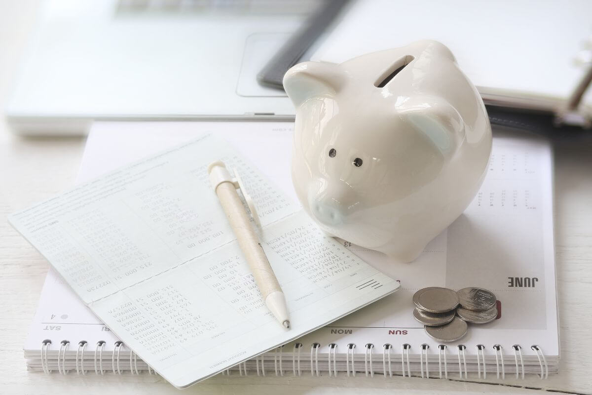 The image tells about a calendar, coins, a piggy bank, a pen, and a bank book which means to automate savings to make it a consistent habit to reaching your financial goals.