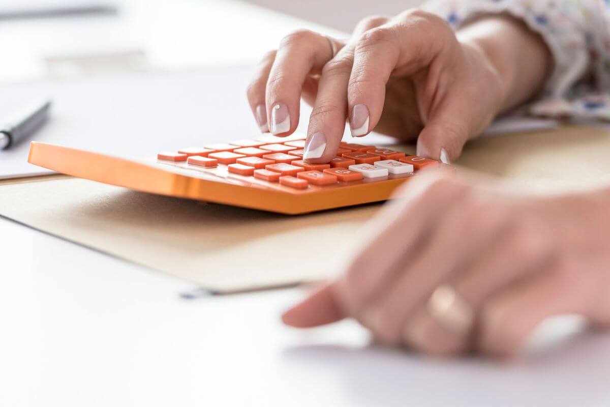 The photo tells about a girl's hand calculating referring to focus on building 3-6 months of expenses to ensure you're financially prepared for anything.