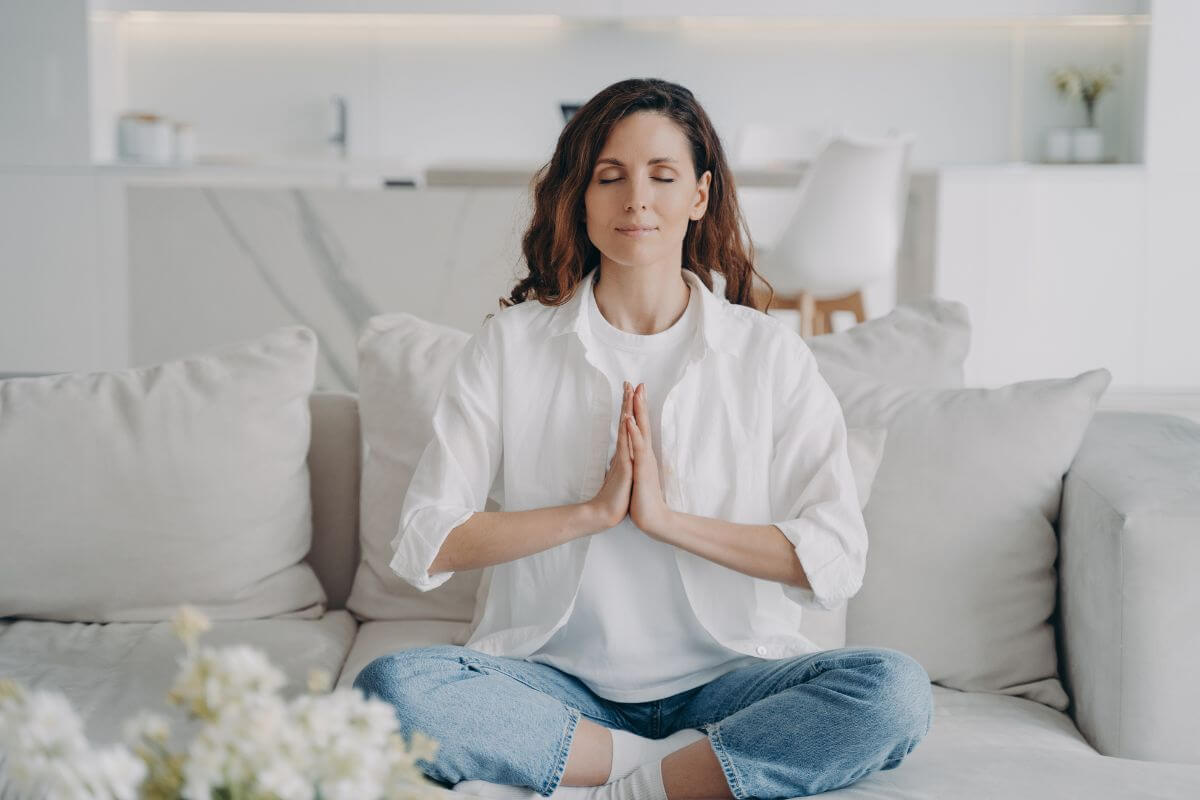 The image tells about a girl doing breathing yoga exercises on the couch which means taking proper steps to reduce your stress level with money and help you feel more in control.