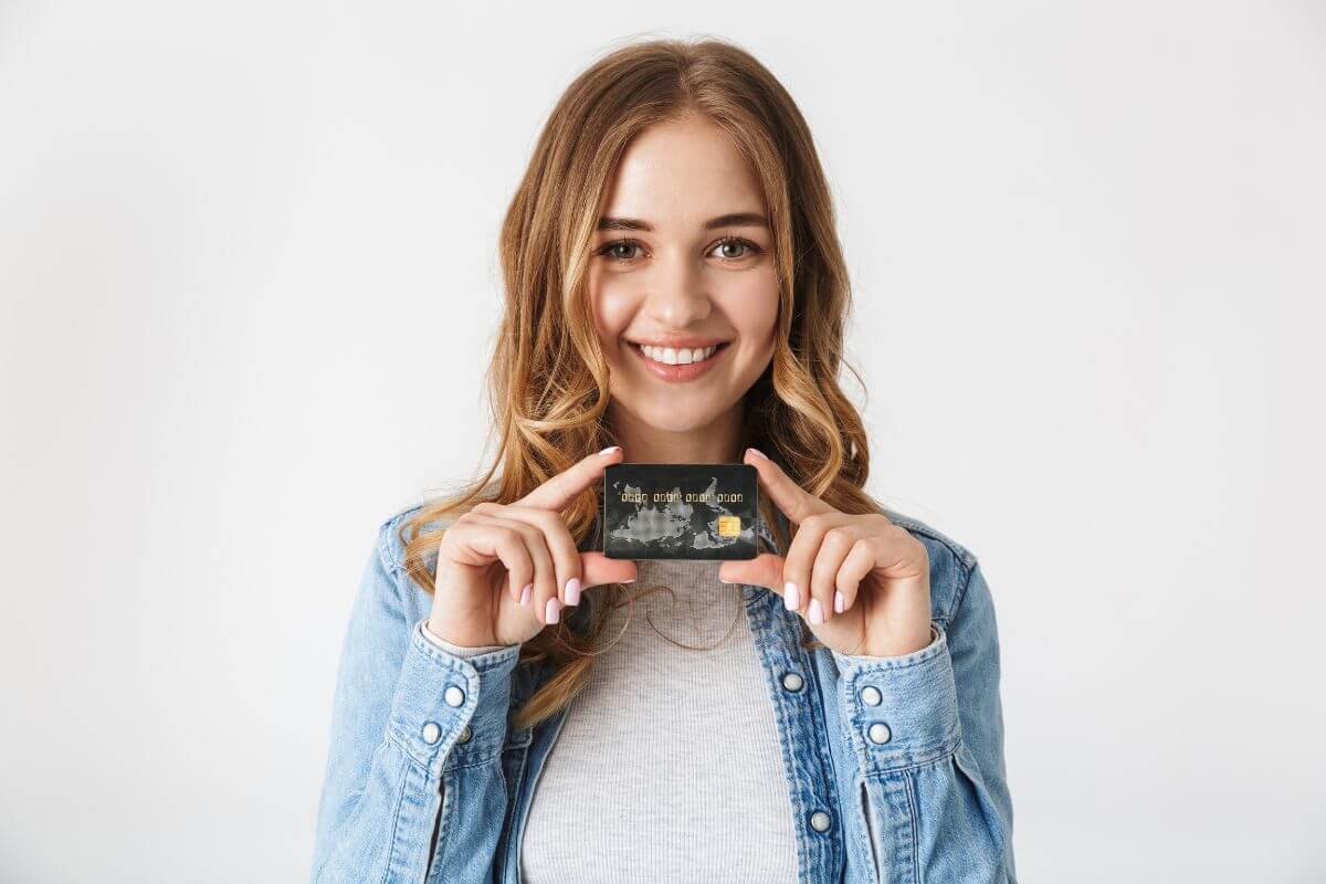 The photo tells about a girl holding a credit card which means to avoid credit card debt by paying off balances keeping your from overspending.