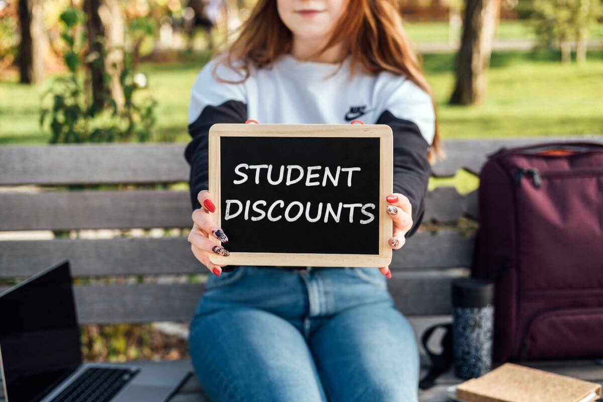 The photo tells about a bag, a laptop, and a girl holding a blackboard with chalk notes referring to using student discounts for everyday purchases helps to stretch your money on food and more.