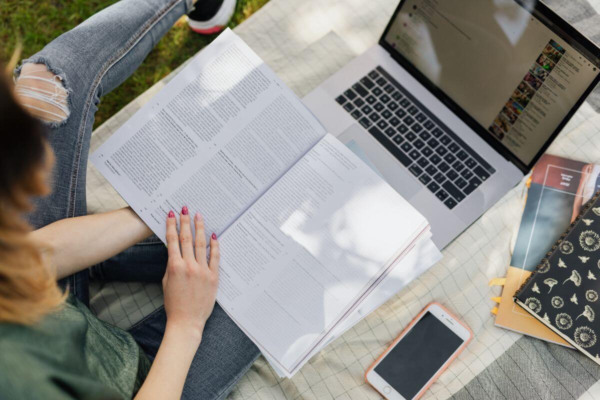 The photo shows a phone, notebook, a laptop, and a student reading a book which refers to looking for affordable alternatives to expensive textbooks to save hundreds of dollars each semester.