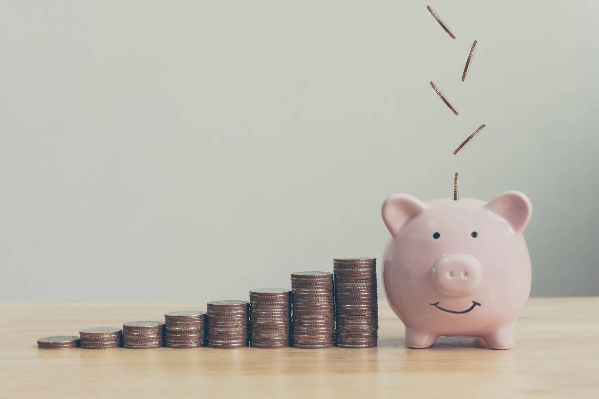 The picture shows stock coins and a piggy bank with coins indicating that setting specific savings goals each month for retirement contributions keeps you focused and motivated.