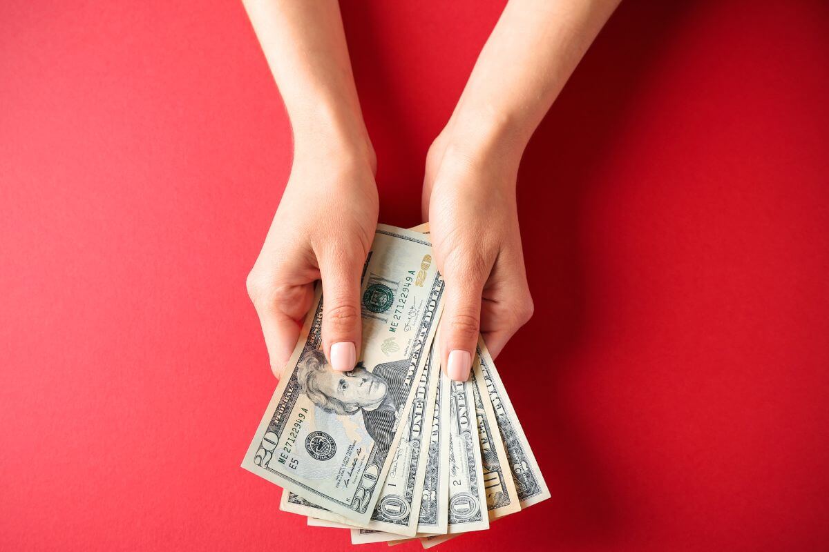 The photo shows a girl's hand holding dollar bills which means to set aside a percentage of income each month that helps you build wealth and prepare for life after college.