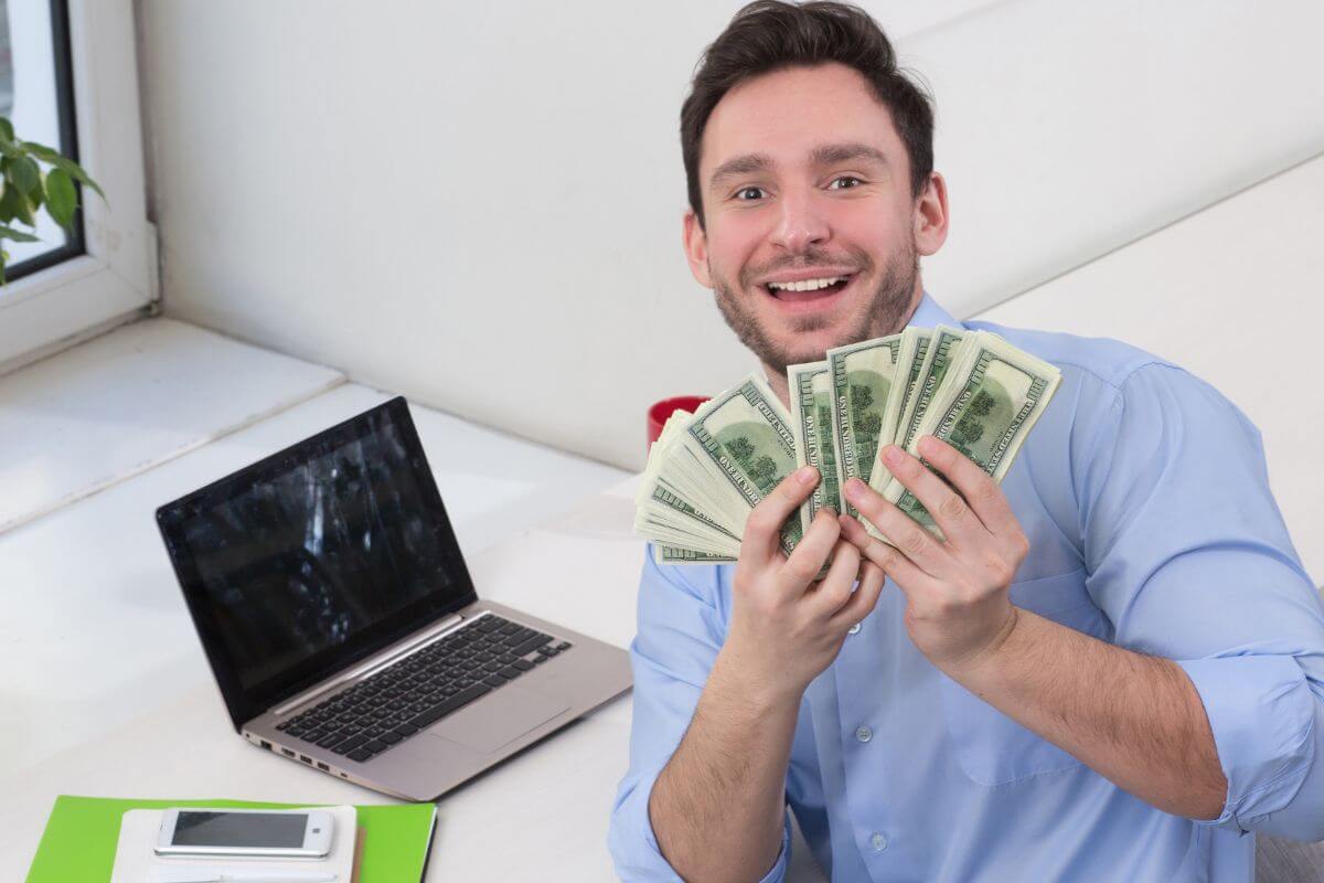The image of a phone, notebooks on the table, a laptop, and a man showing his salary which means working towards a freelance job to increase income for savings or fun.