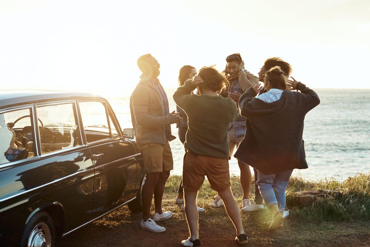 The photo of a car and a group of friends enjoying at the seaside indicating to look for free or low-cost entertainment with friends to stick to your budget.