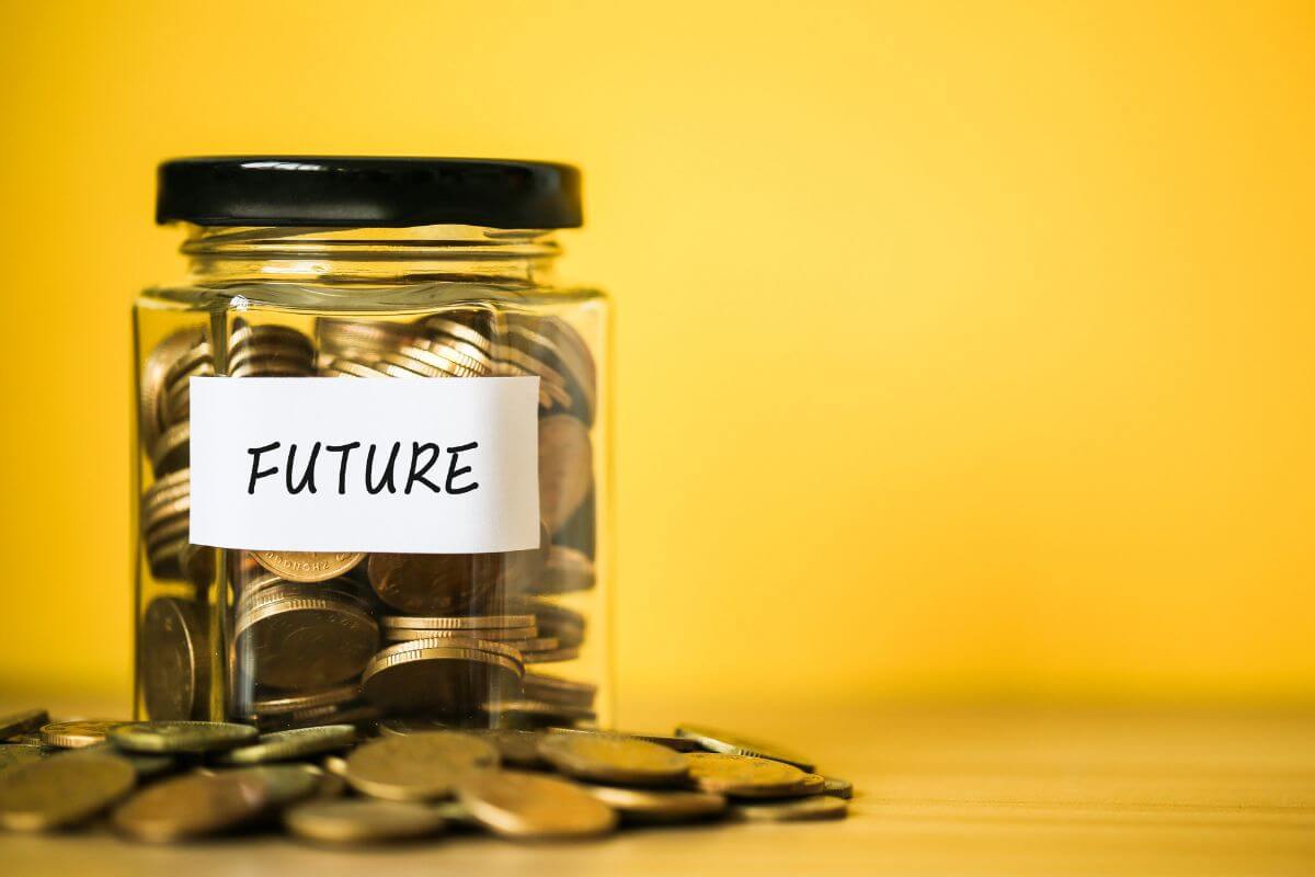 The photo shows coins on the table a jar filled with coins and a note referring to saving for future goals with a clear plan makes these goals more achievable and less stressful.