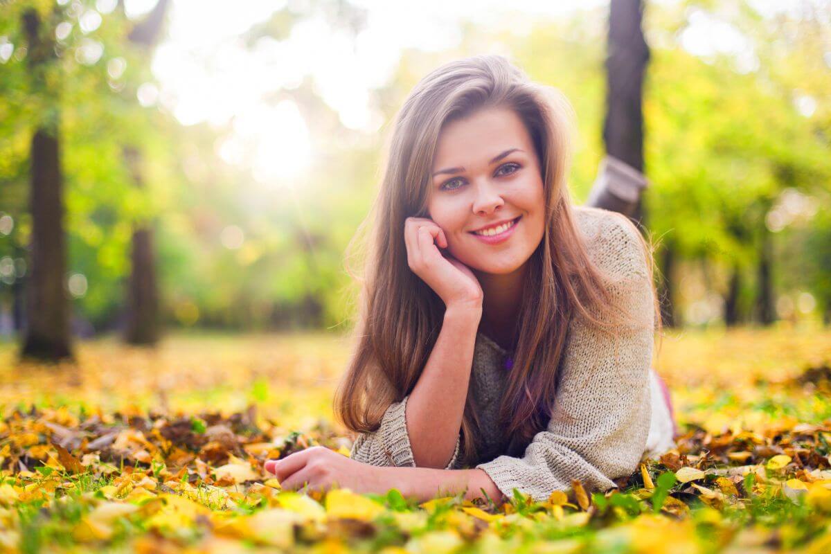 The photo of a girl lying on the grass and smiling which refers to developing the habit of living below your means is a step toward reaching financial freedom as you grow older.
