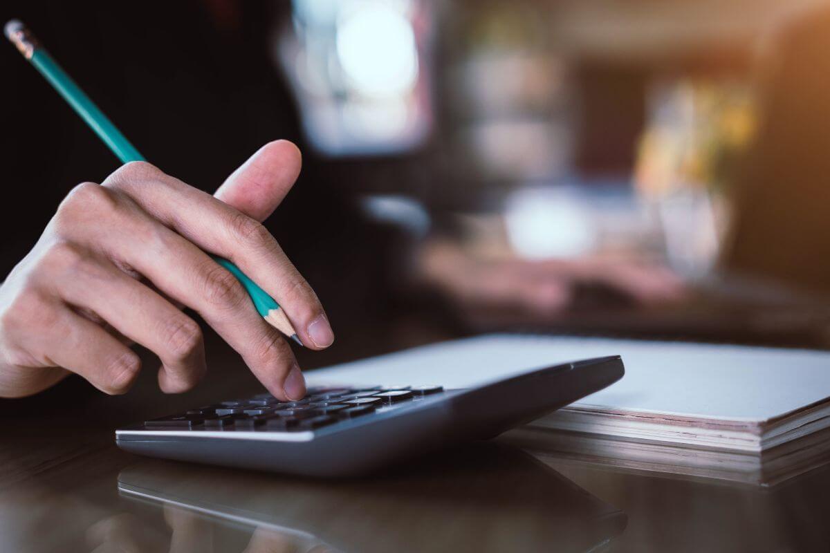 The picture of a notebook and a girl's hand calculating while holding a pen indicating to avoiding a budget makes it easy to overspend your money.