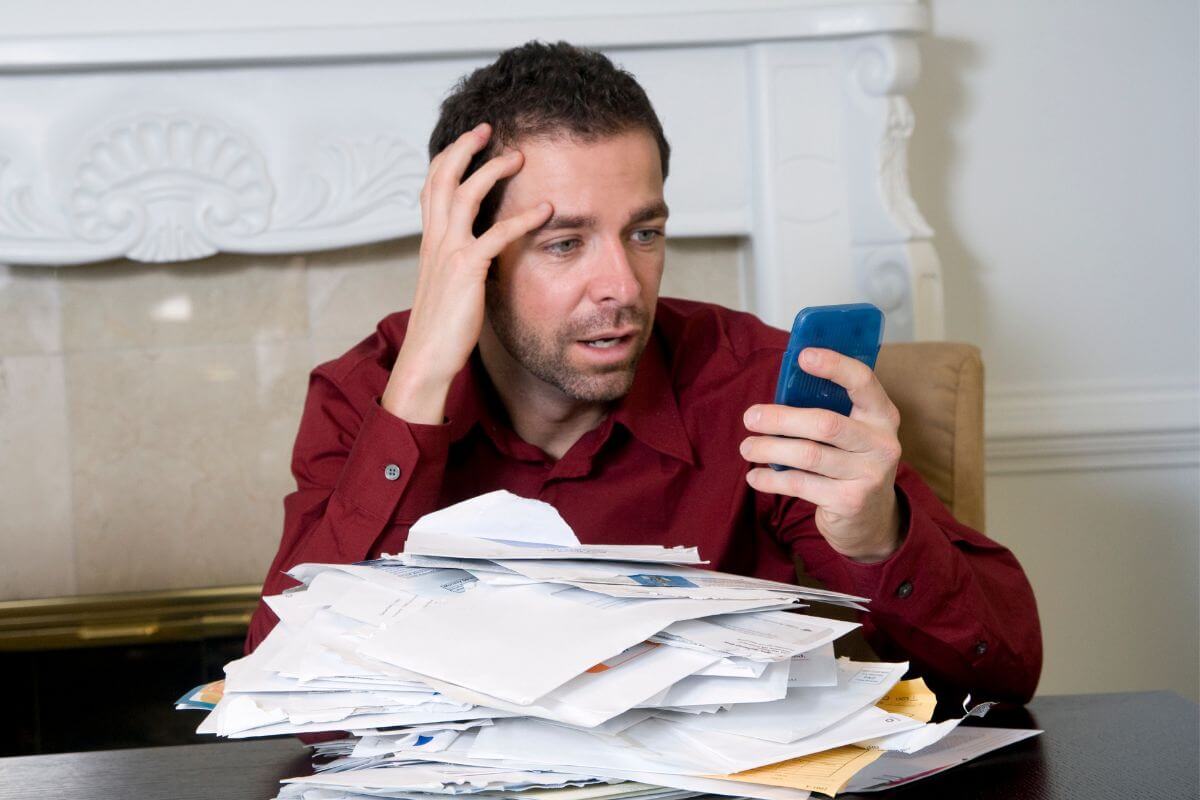 The picture shows papers on the table and a man holding a phone, which refers to being heavily in debt, which limits one's financial freedom and burdens.