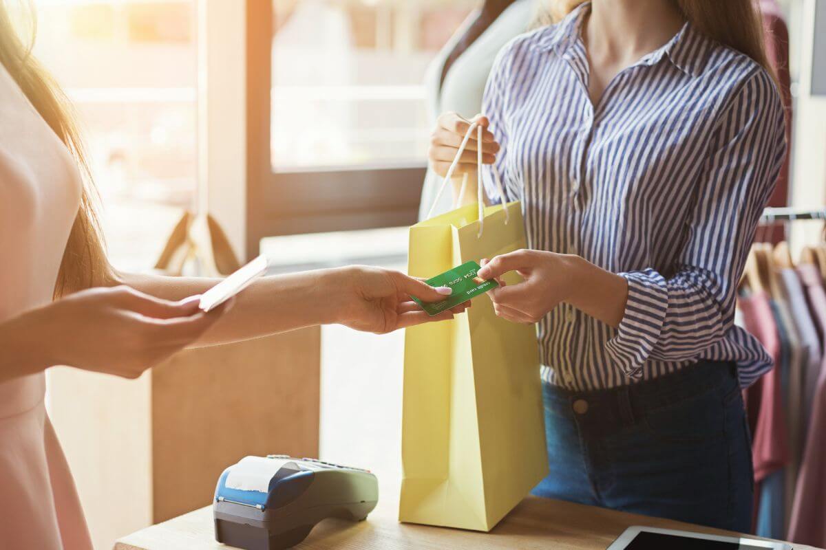 The photo shows a customer giving her credit card to the customer holding her order at the store indicating that spending too much on wants keeps you from reaching your goals.