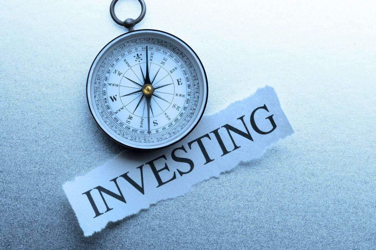 The photo shows a compass and a piece of paper with a note indicating that not investing means missing out on long-term growth.