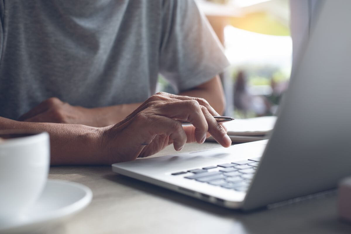 The picture of a coffee, a notebook, and a man's hand holding a pen while using a laptop to search and learn other ways you make money mistakes to improve and reach financial freedom.