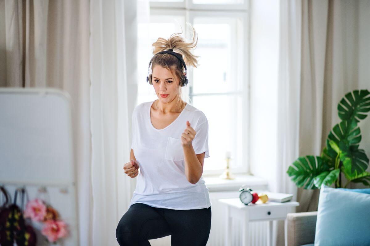 The photo tells about a plant, a couch, home stuff, and a girl doing an exercise at home which refers to swap expensive hobbies with a budget-friendly ones can mathat ke a big difference in your expenses.