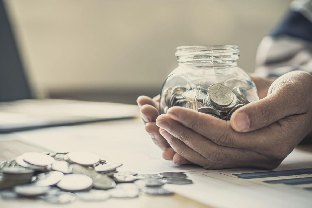 The picture of coins on the table and the man's hand holding a jar filled with coins means setting up fun or reward budgets so you are motivated without overspending.