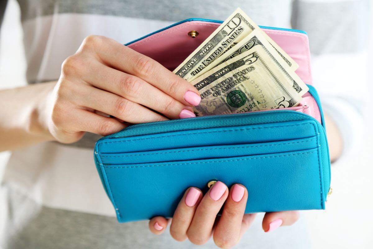 The image of a girl's hand holding a wallet and putting the dollar bills inside of it which means creating a no-spend challenge can help you rethink your spending and build stronger money habits.