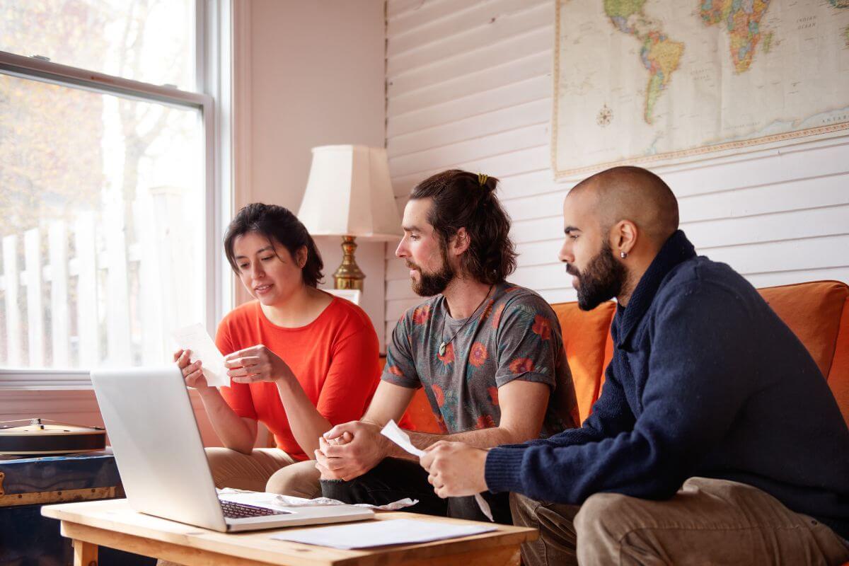 The image shows a laptop, paper on the table, and a group of friends holding papers which means setting a budget with friends and staying accountable can make the process more effective and fun.