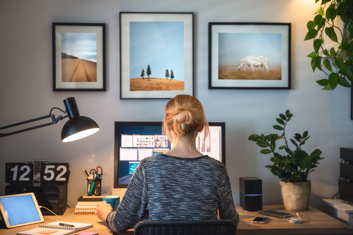 The image tells about wall frames, plants, a lamp, a tablet, and a girl working on her computer indicating to work to be the millionaire from no money and Building income streams to work your way to millionaire sttatus.