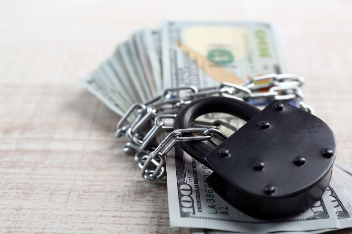 The photo shows dollar bills with a lock and chains indicating to have a financial safety net that protects you from setbacks and keeps you moving toward independence.