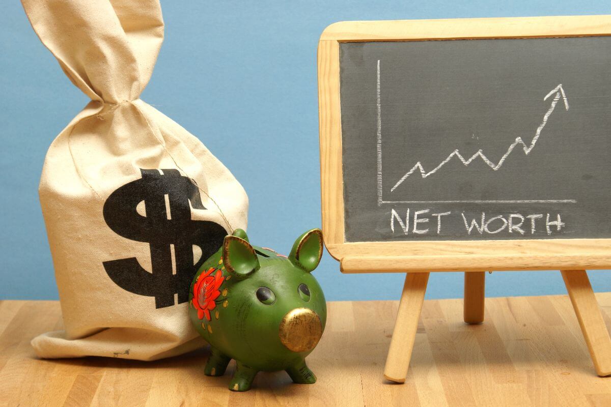 The photo shows a bag with a dollar sign, a piggy bank, and a blackboard with notes referring to tracking your net worth regularly to see how far you've come and improving your money habits.
