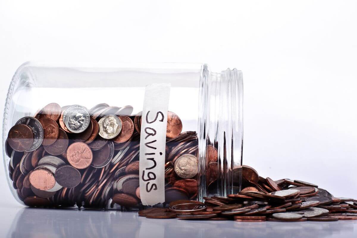The photo shows a jar filled with coins and a note referring to setting a small monthly savings goal that prepares you for bigger financial goals.