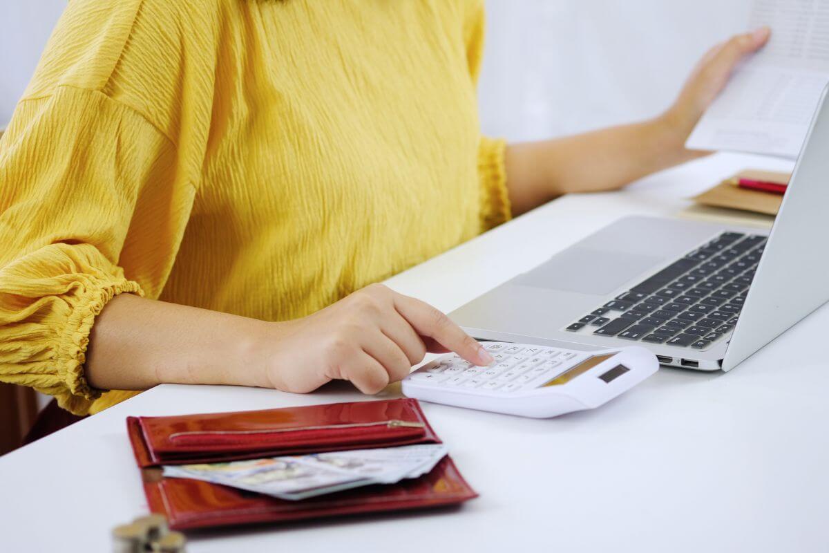 The image shows a wallet with dollar bills, coin stocks, a laptop, and a girl using a calculator while holding a bank book indicating that borrowing money can limit the lender's ability to manage their own finances and make it harder for them to cover their own needs.