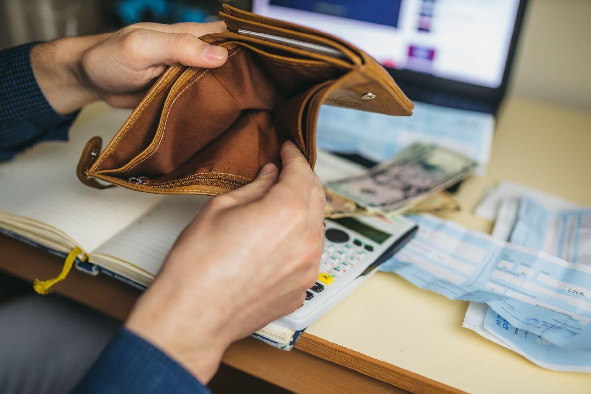 The picture tells about paychecks, a calculator, a notebook, a laptop, dollar bills, and a man's hand opening an empty wallet which refers to borrowing money and often avoids addressing underlying financial habits and delays to address long-term problems.