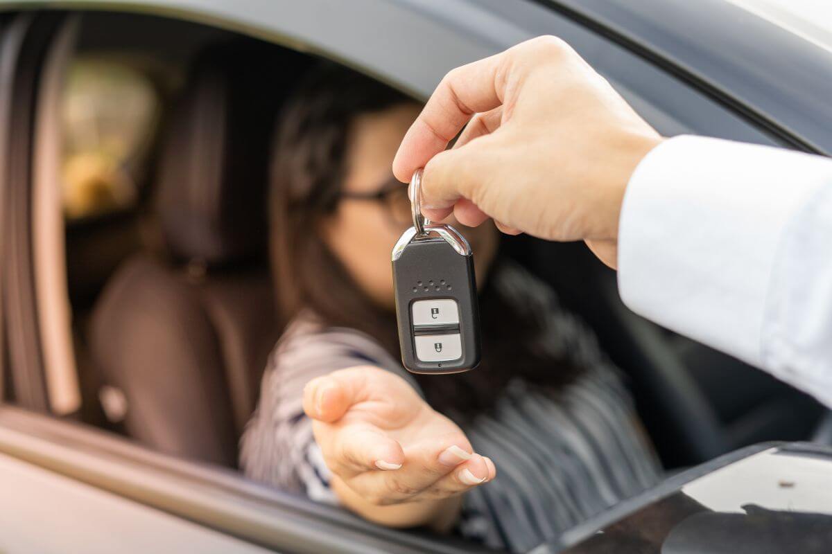 The photo shows a man's hand giving the key car to the girl in the driving seat which means to rent out your car on a car-sharing app to earn passive income without much effort.