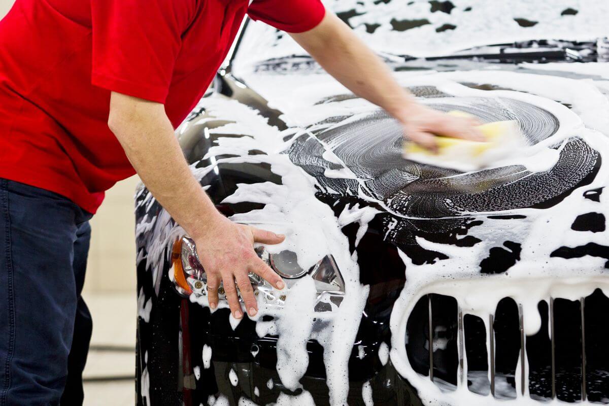 The image shows a man cleaning a car with a sponge and soap referring to starting a mobile car-washing service to make quick cash in your local area.