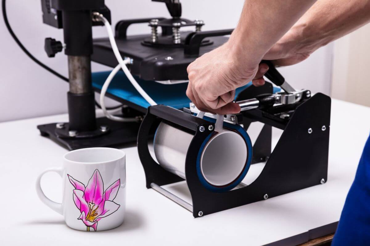 The image shows a machine operated by the man used to print mugs and a finished product mug on the table indicating to creation and sale of print-on-demand products to make passive income without holding inventory.