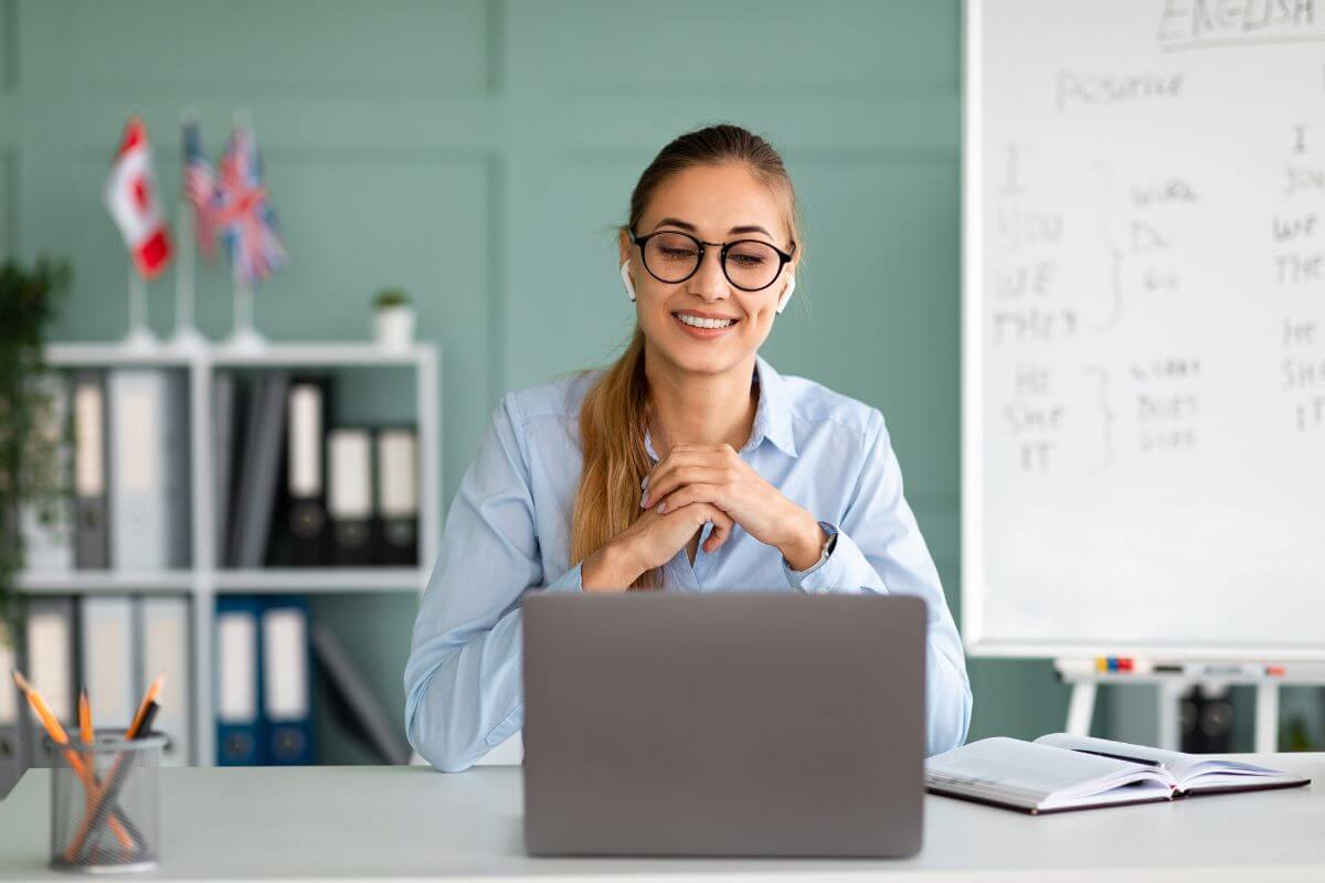 The image tells about a whiteboard with notes, a notebook with a pen, files on the book shelve, flags, and a girl looking at the laptop to host online tutoring sessions for students to earn money while helping others succeed.