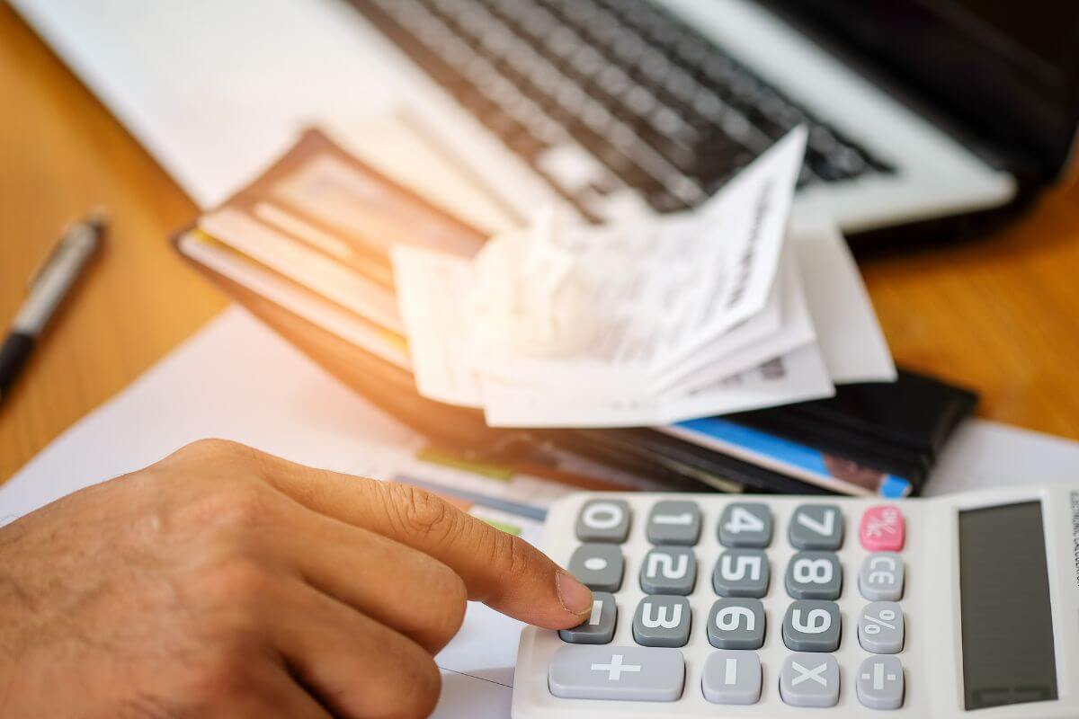 The image of a laptop, a pen, a wallet with cards, receipts, and a man's hand calculating to subtract expenses from income to make adjustments so you can stay on track.