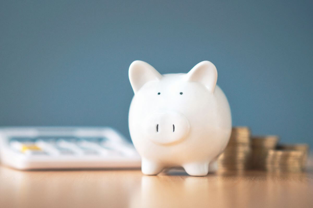 The image tells about coin stocks, a calculator, and a piggy bank referring to plan for savings from your income to build a safety net and reach long-term financial goals.