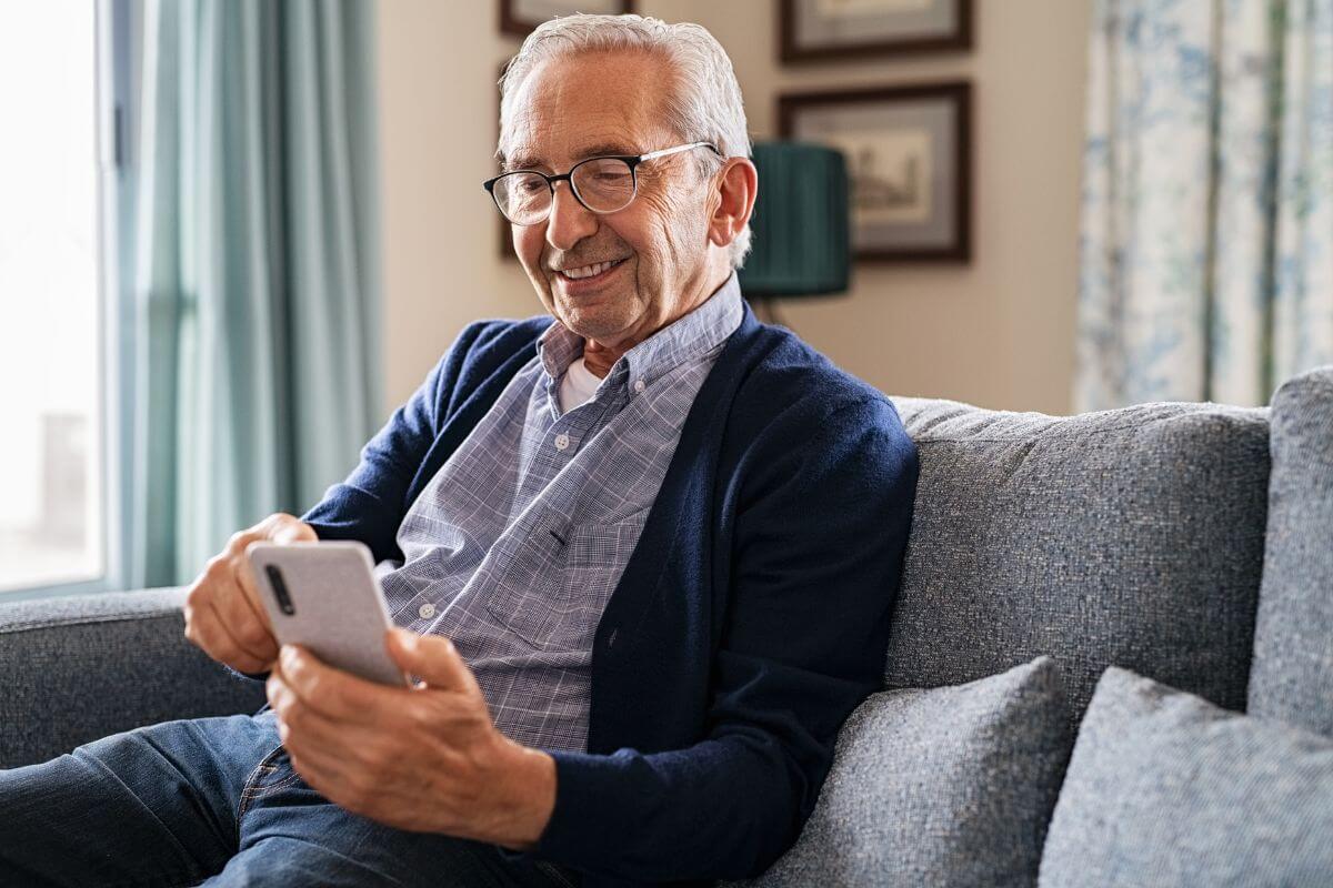 The picture shows a senior sitting on a couch while using a phone which refers to switch to a senior phone plan helping you stay connected without spending more than you need.