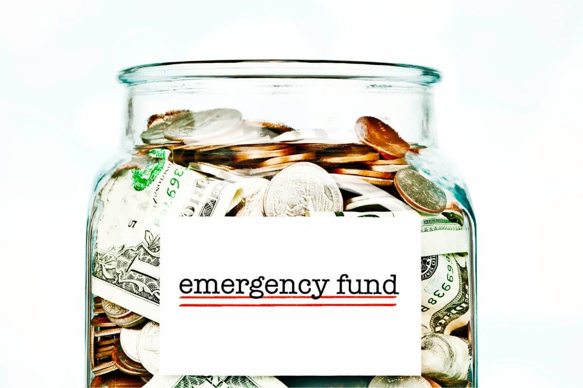 The photo tells about a jar filled with dollar bills, coins, and a note which means that building an emergency fund can keep you from falling into debt when surprise expenses pop up.