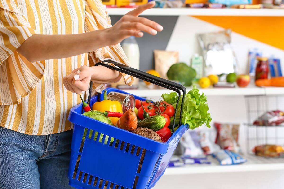 The image shows a girl carrying a basket full of essentials at the store indicating that focusing on needs over wants lets you save more.