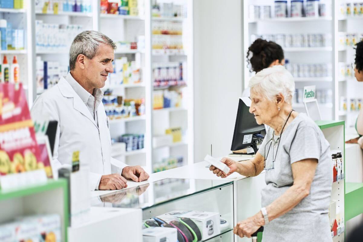 The photo of a pharmacist assisting the senior in line at the pharmacy referring to save on prescription medications with senior discount programs to lower the cost of necessary medications.