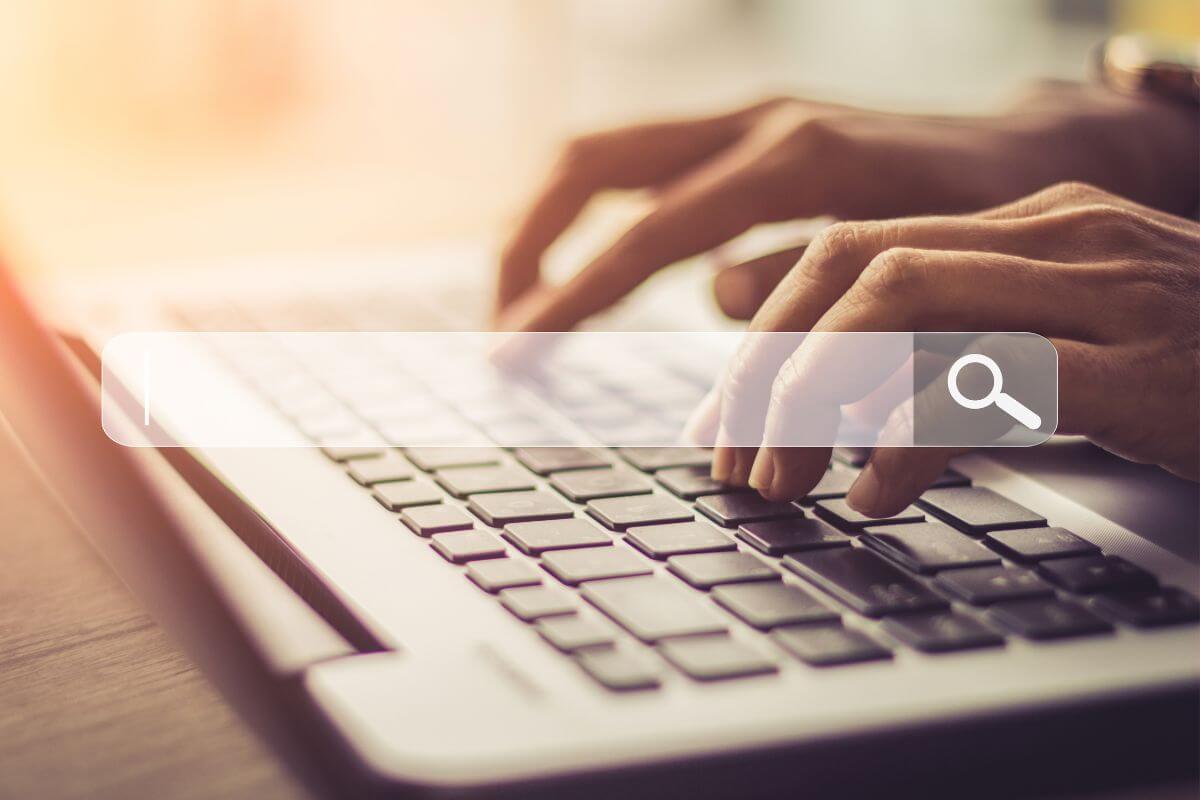 The mage shows a man's hand typing on the laptop and a search icon on screen which means to find specific instructions on ways to stop living paycheck to paycheck to create a more secure future.