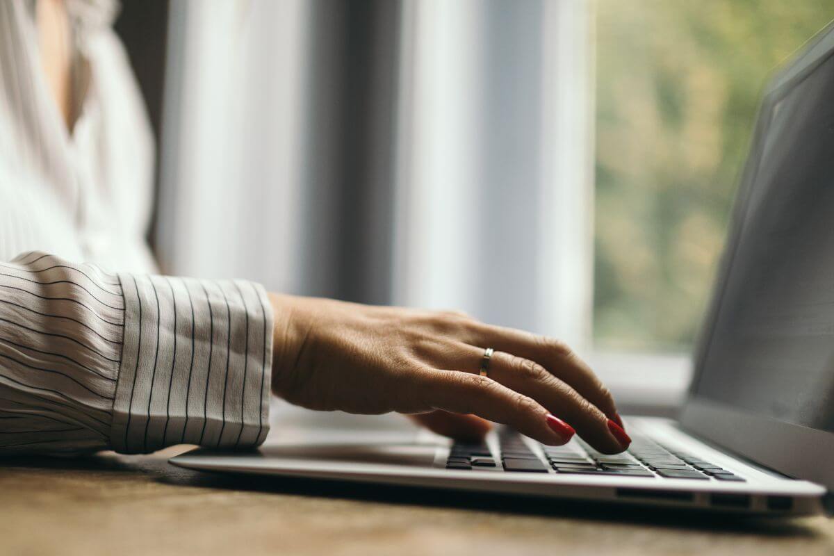 The picture of a girl's hand typing on a laptop which means to offer virtual assistant services to earn money from home and build long-term client relationships.