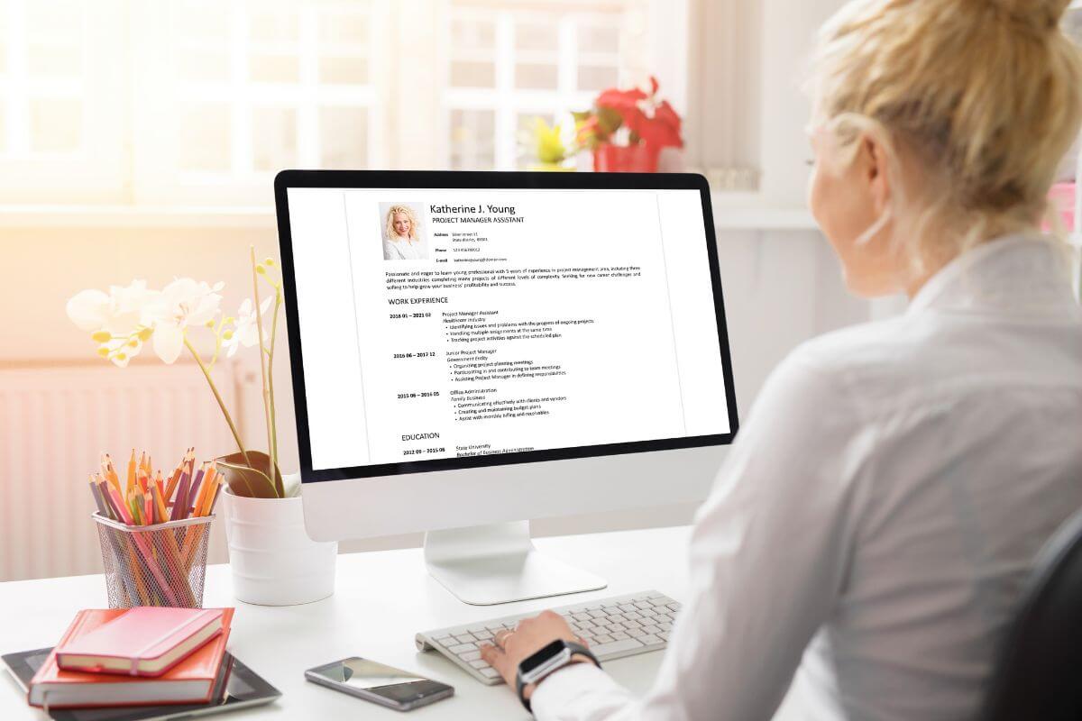 The photo of a container with pens, notebooks, a tablet, a phone, and a girl using a computer desk indicates to offer professional resume writing services that can be a profitable way to use your writing skills.