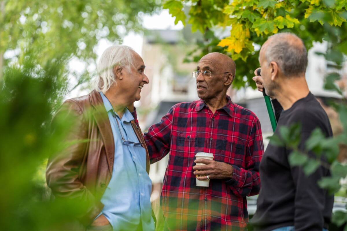 The image shows a senior talking to his neighbors in the backyard which means barter services with local communities to reduce expenses while fostering community connections.