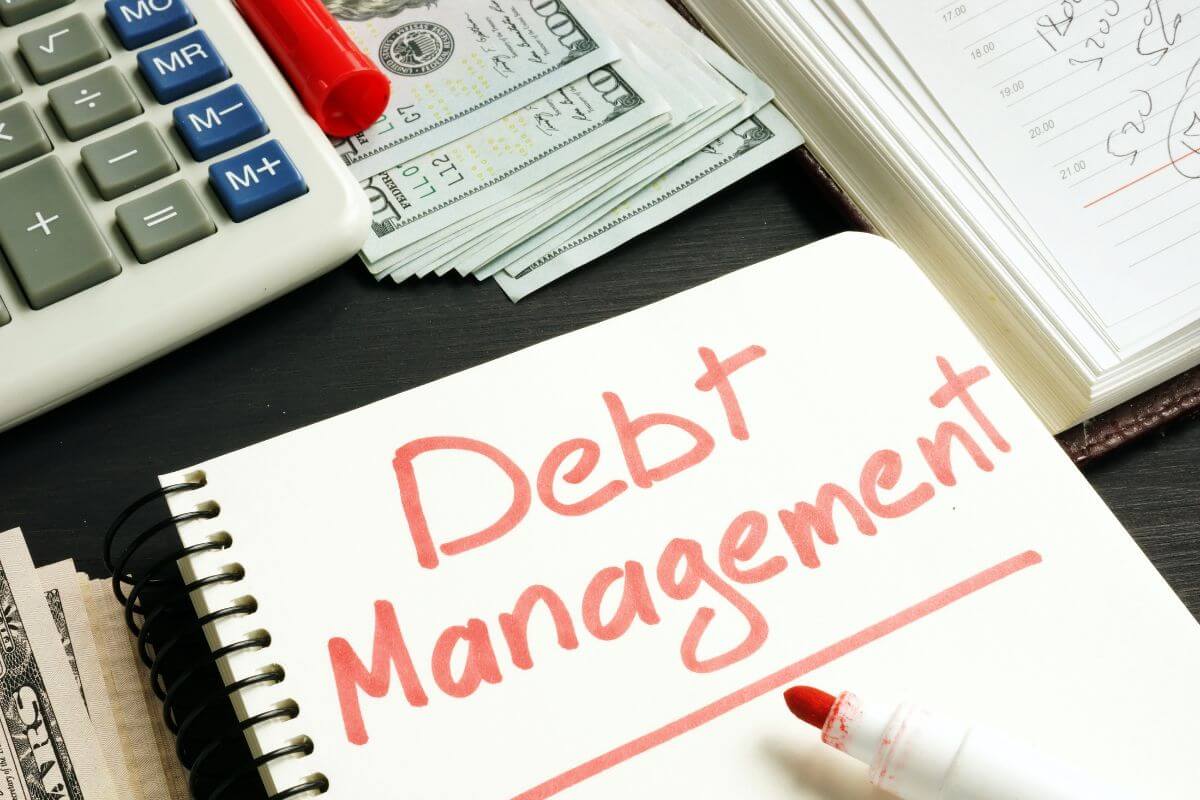 The image shows a calculator, dollar bills, a notebook, a marker, and a notebook with notes which means to manage your debt effectively to grow your net worth.
