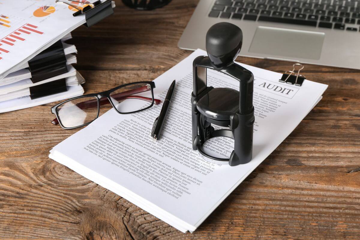 The picture shows documents on the table, a laptop, an eyeglass, a pen, a stamp, and papers referring to the offer of mobile notary services in your area that can bring in steady income with minimal time commitment.