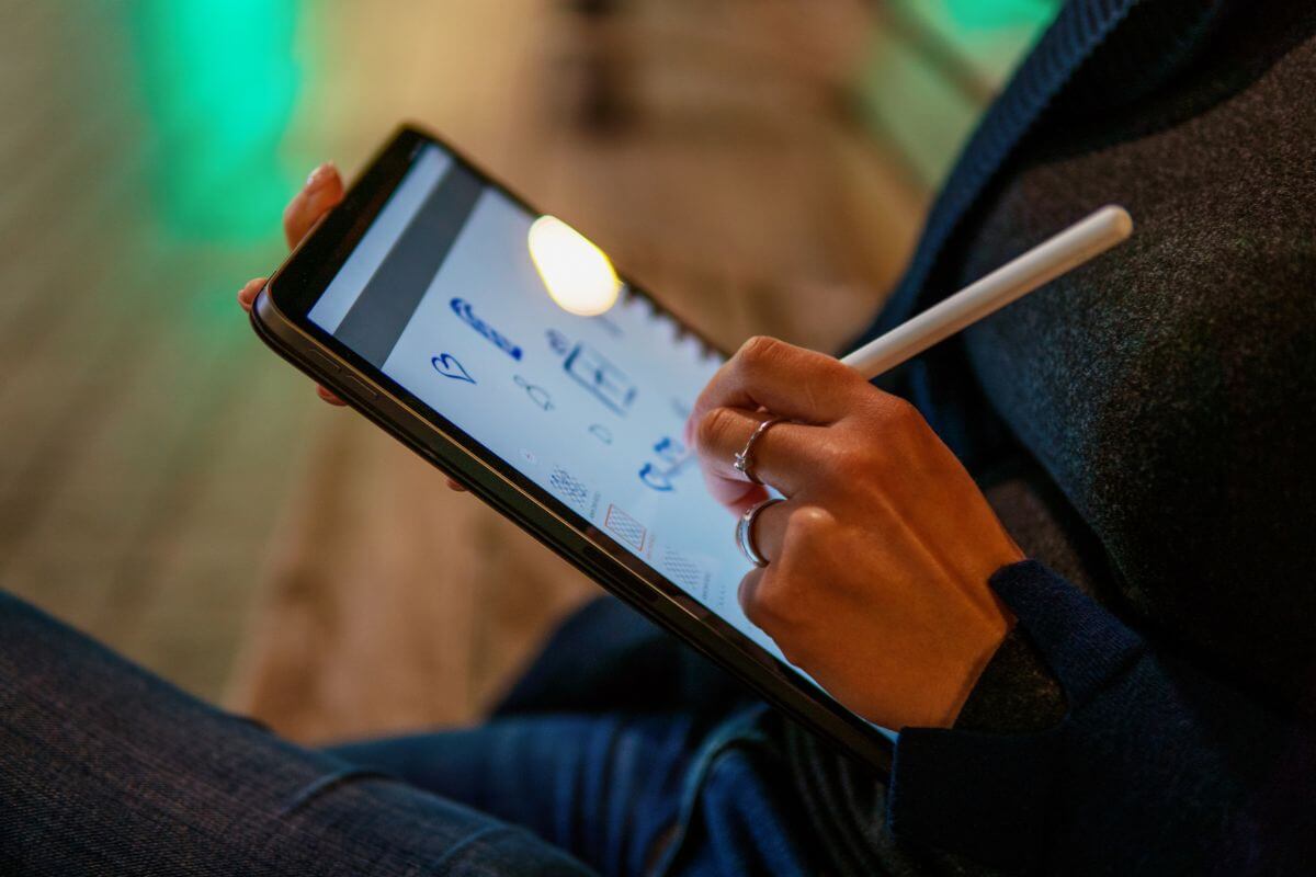 The picture of a girl drawing on the tablet indicates creating and selling digital art on Canva to make money and a flexible side hustle you can do from home.