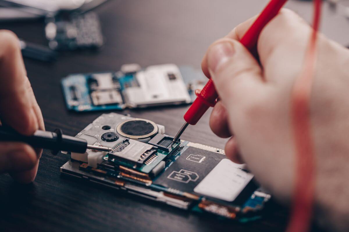 The picture tells about a man's hand repairing a phone which means setting up a mobile phone repair service that can be a steady source of extra money.