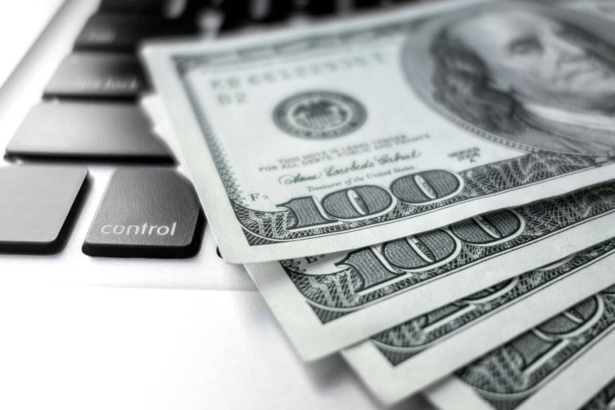 The photo shows a laptop and dollar bills which refers to finding more ways to make quick money to make extra cash when you need it most.
