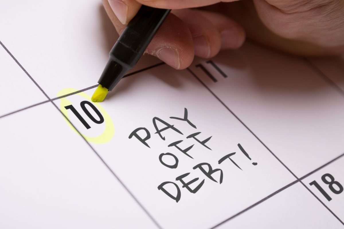 A man's hand marking a calendar with pay off debt note.
