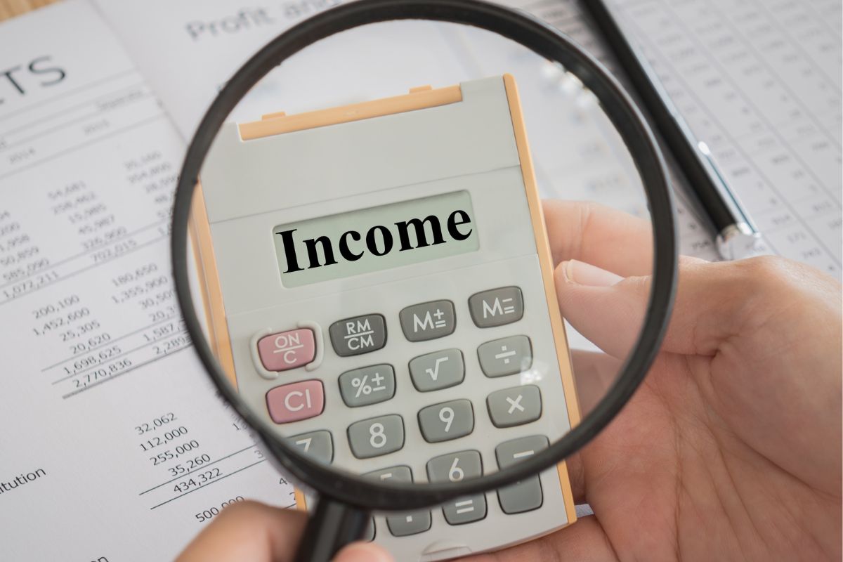 A man's hand holding a calculator with income wording.
