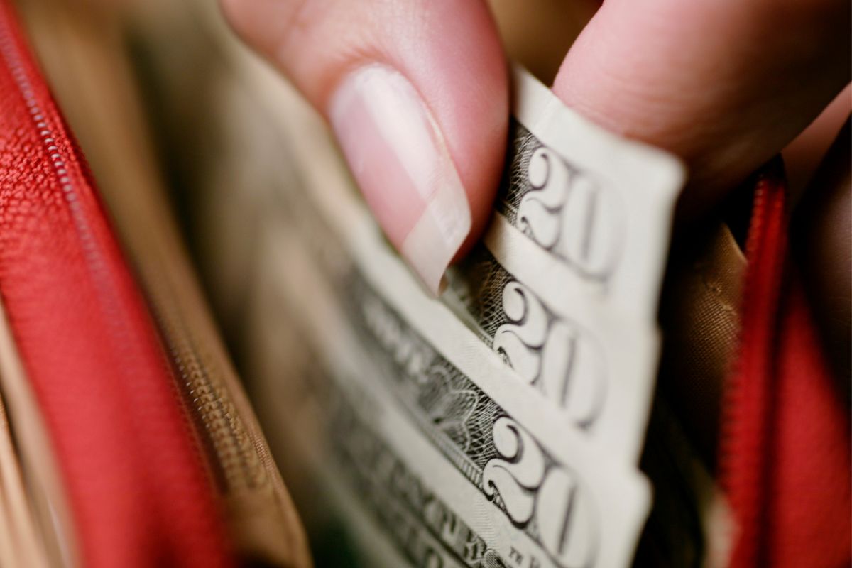 Image of a woman's hand pulling money from her wallet.