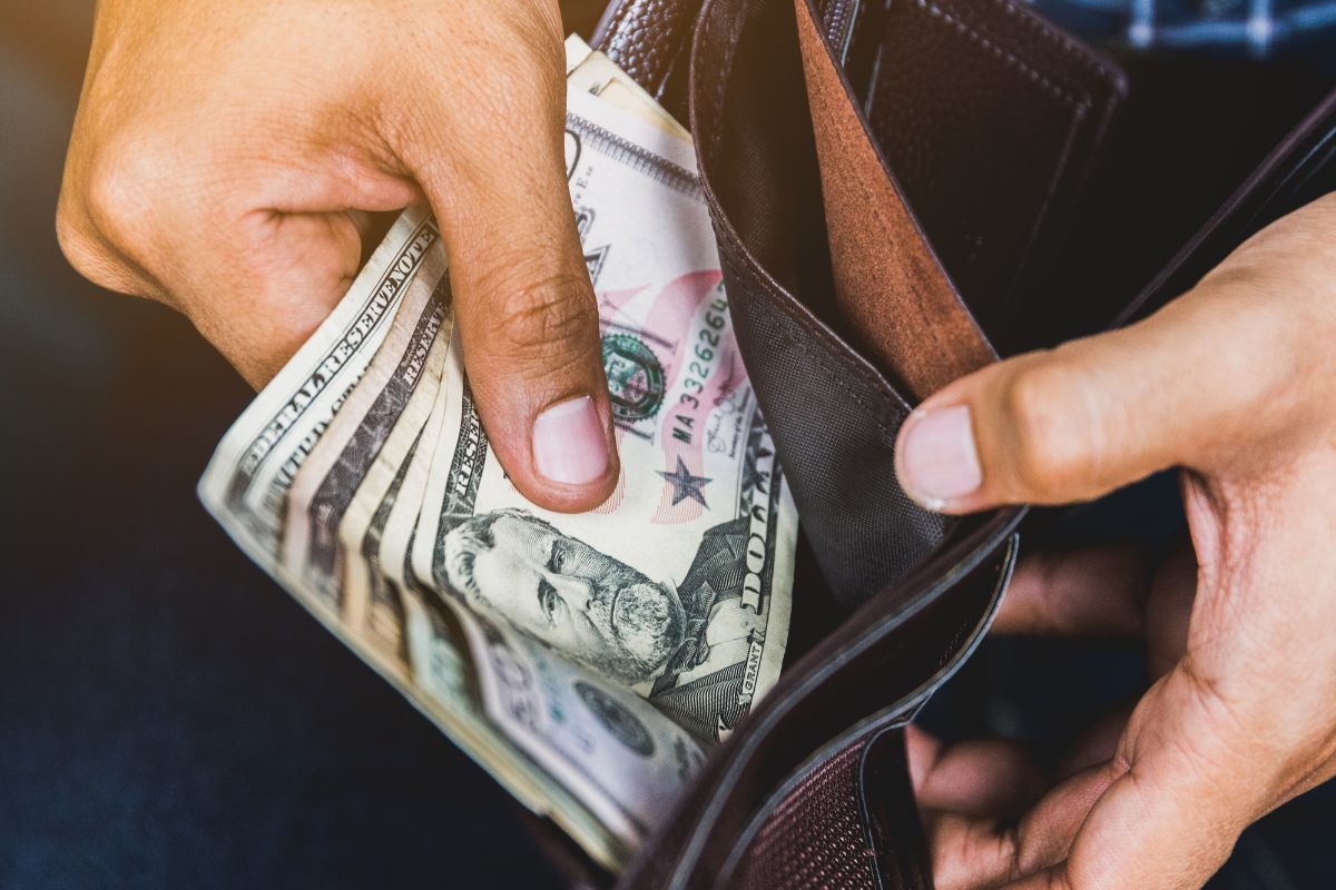 Image of a man's hand putting her money in his wallet.